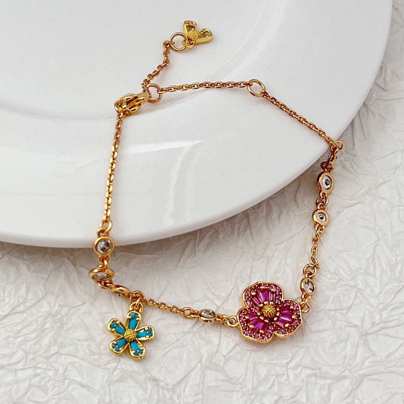 Bracelet displayed on a soft moss green or linen background, highlighting the mix of floral and leaf charms. Alt: “Kate Spade Yellow Gold Plated Flowers & Plants Bracelet – Botanical Charm Jewelry.”