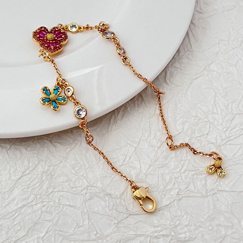 Bracelet displayed on a soft moss green or linen background, highlighting the mix of floral and leaf charms. Alt: “Kate Spade Yellow Gold Plated Flowers & Plants Bracelet – Botanical Charm Jewelry.”