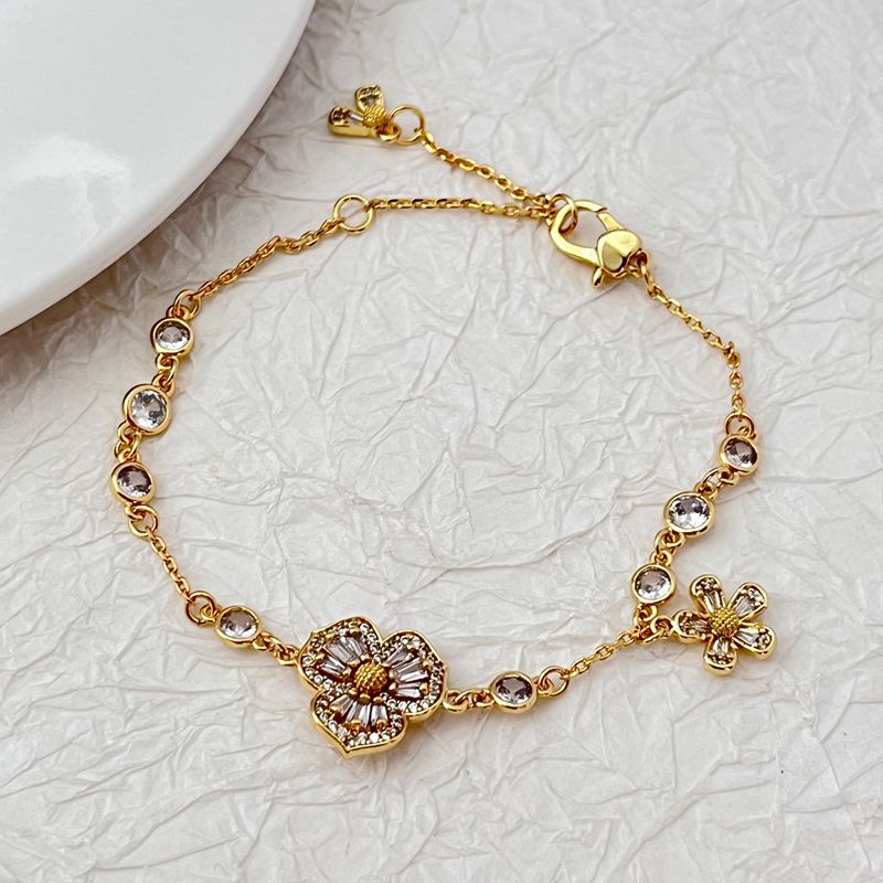 Bracelet displayed on a soft moss green or linen background, highlighting the mix of floral and leaf charms. Alt: “Kate Spade Yellow Gold Plated Flowers & Plants Bracelet – Botanical Charm Jewelry.”
