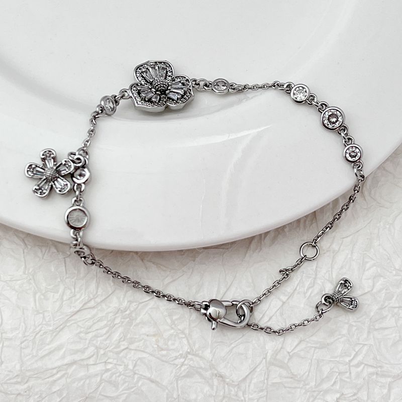 Bracelet displayed on a soft moss green or linen background, highlighting the mix of floral and leaf charms. Alt: “Kate Spade Yellow Gold Plated Flowers & Plants Bracelet – Botanical Charm Jewelry.”