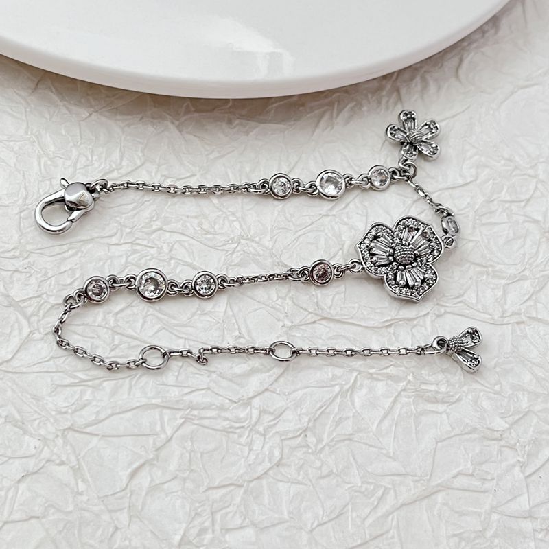 Bracelet displayed on a soft moss green or linen background, highlighting the mix of floral and leaf charms. Alt: “Kate Spade Yellow Gold Plated Flowers & Plants Bracelet – Botanical Charm Jewelry.”