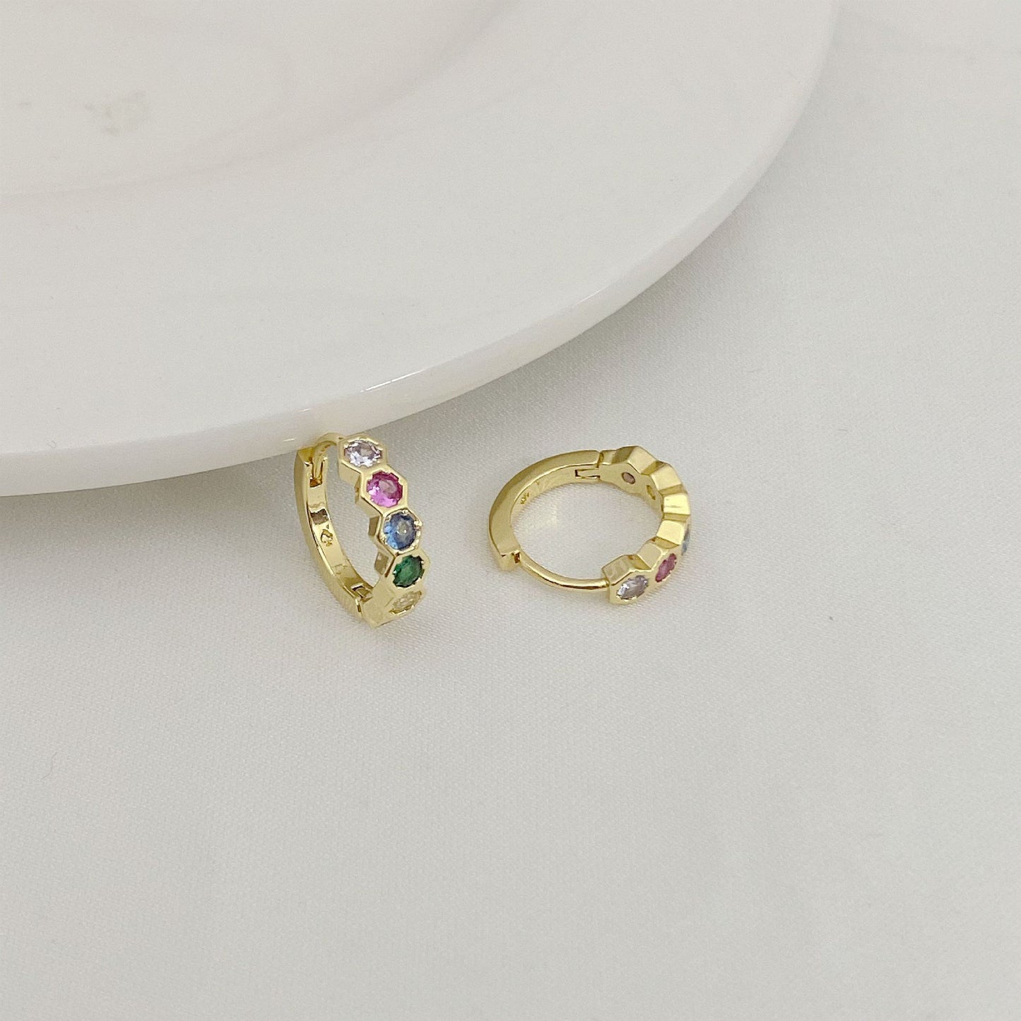 Gold hoop earrings with colorful gemstones on a light gray background