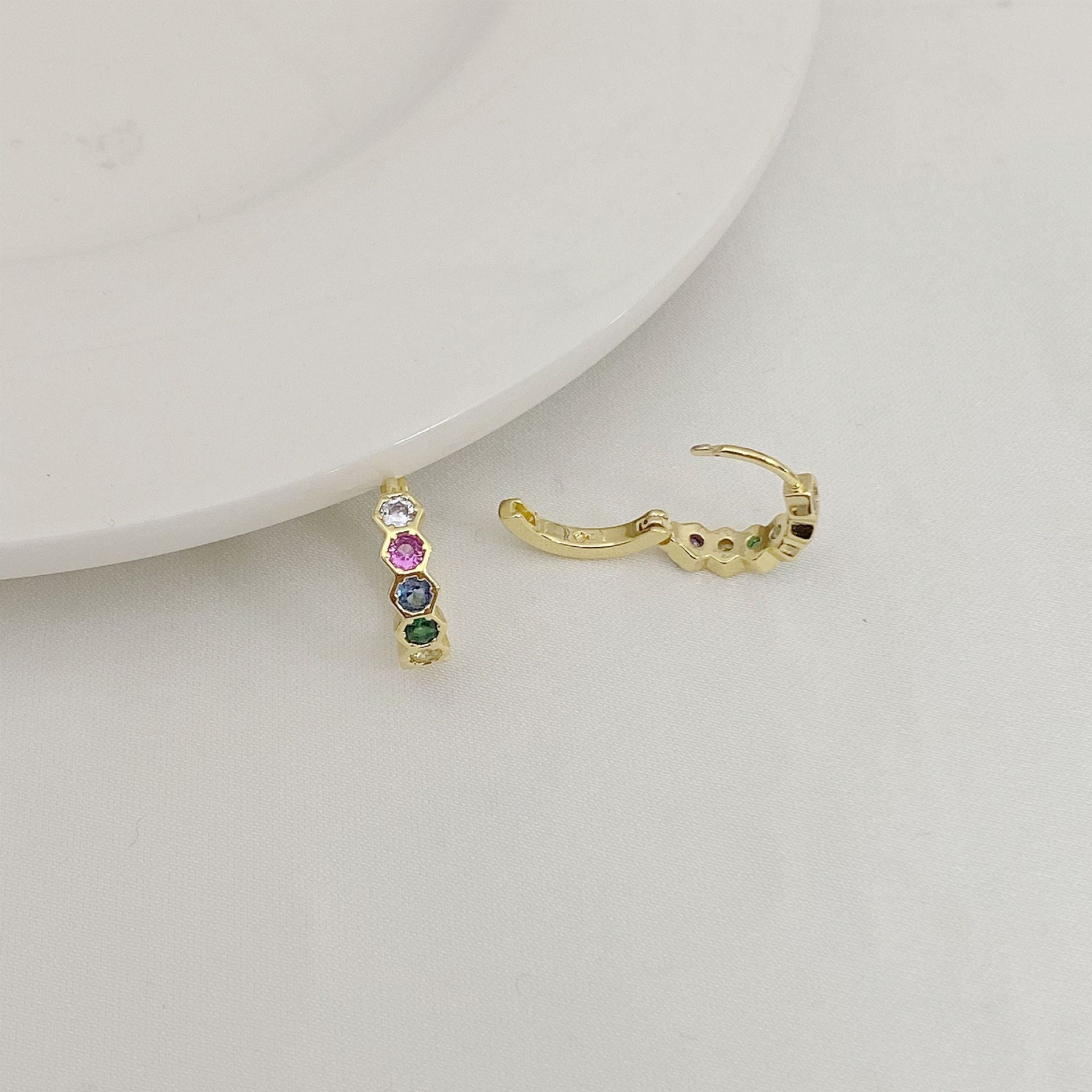 Gold hoop earrings with embedded gemstones on a light gray surface.