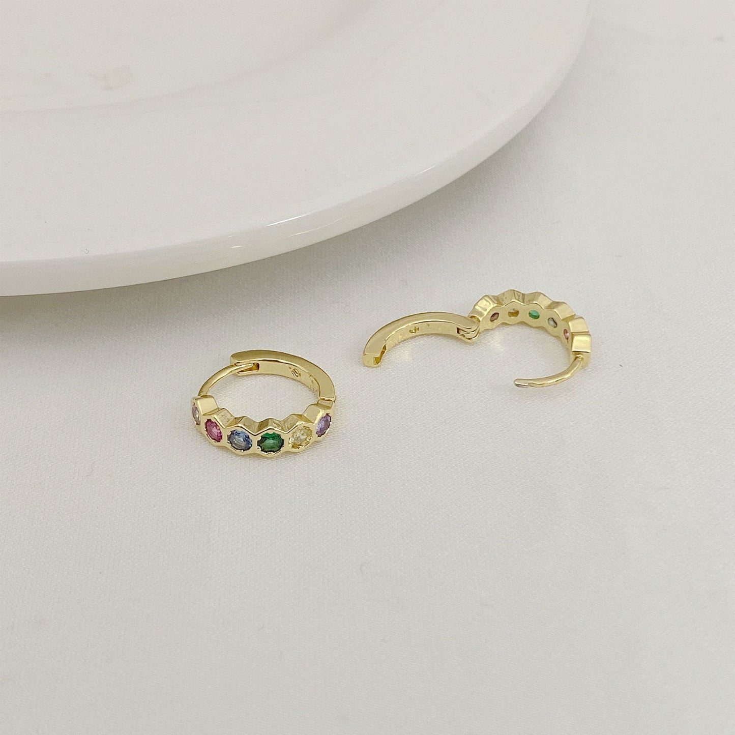Gold hoop earrings with colorful gemstones on a light gray surface.