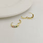 Gold hoop earrings with colorful gemstones on a light gray background