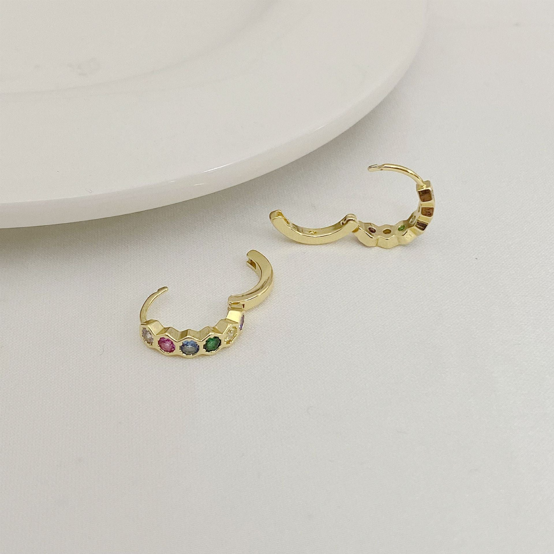 Gold hoop earrings with colorful gemstones on a light gray background