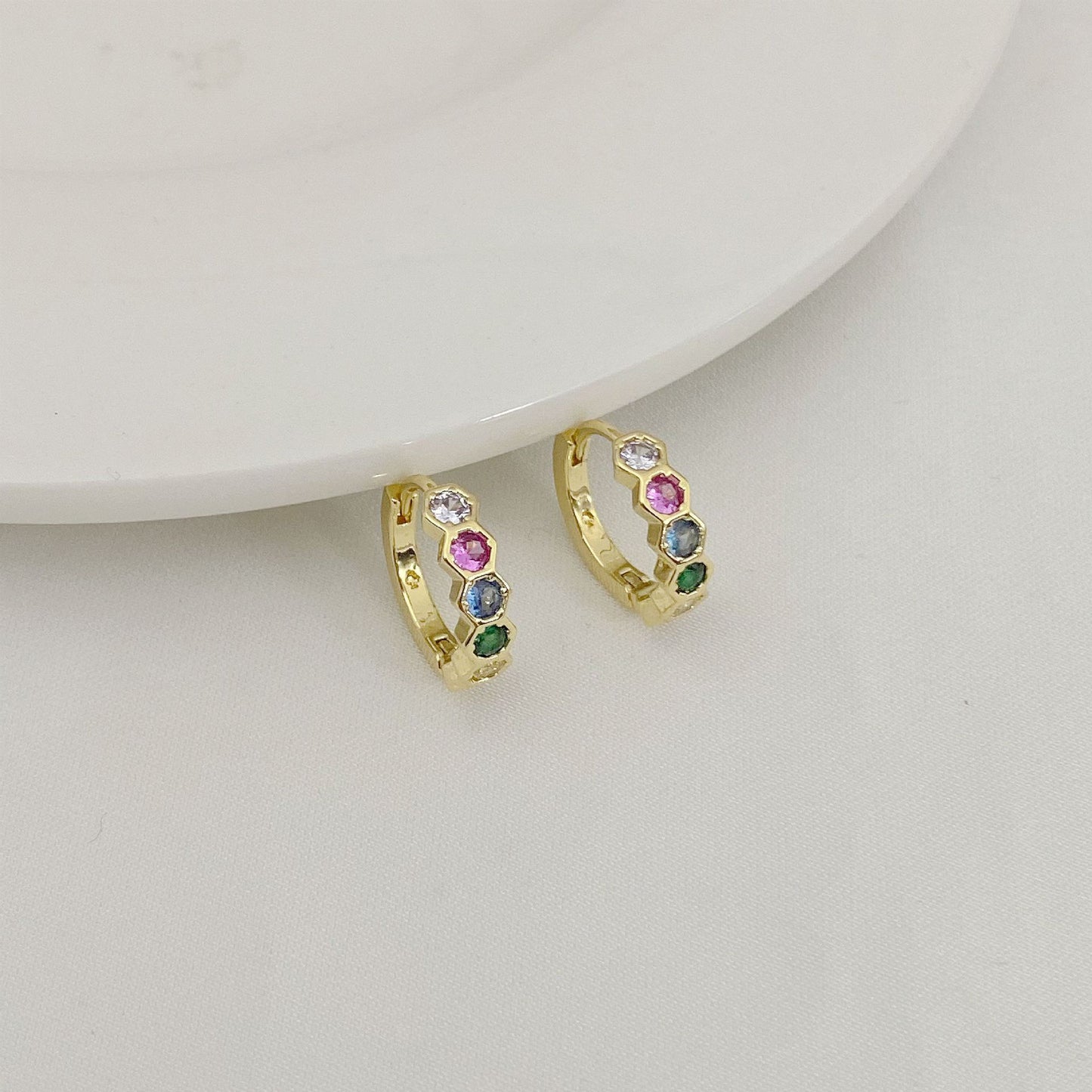 Gold hoop earrings with colorful gemstones on a light gray background