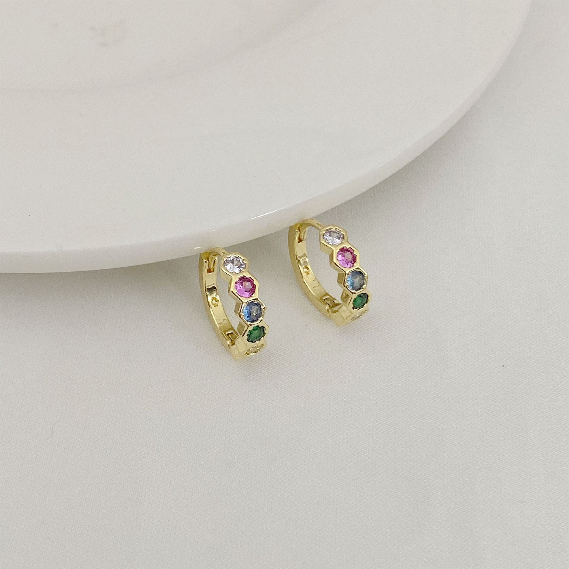 Gold hoop earrings with colorful gemstones on a light gray background