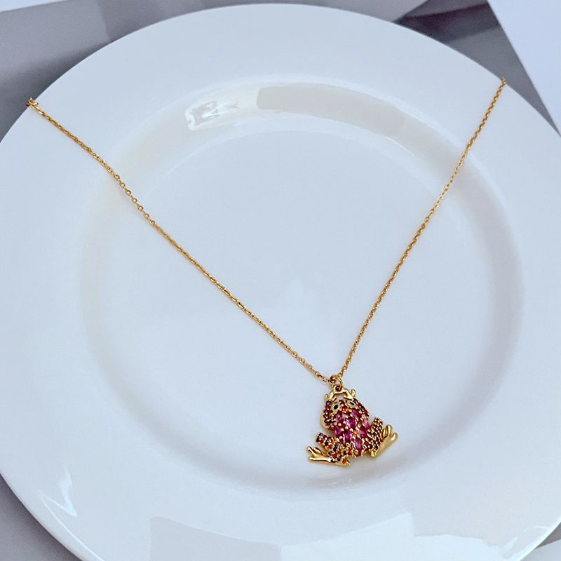 Necklace displayed on a soft green or natural-toned background, highlighting the frog pendant’s shape and crystal details. Alt: “Kate Spade Pave Frog Drop Pendant Necklace – Whimsical Crystal Animal Jewelry.”