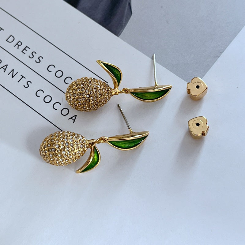 Earrings displayed side by side on a soft linen or farmers' market-inspired background, showcasing the mismatched pear and lemon charms. Alt: “Kate Spade Pear Lemon Earrings – Enamel Citrus & Pear Drop Jewelry.”