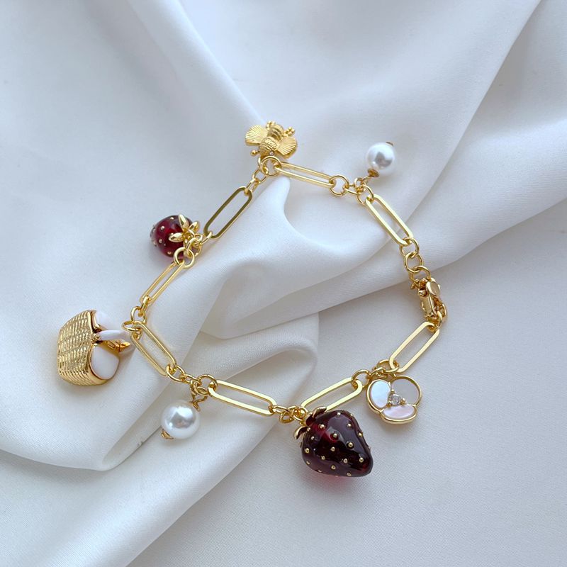  Bracelet displayed on a red gingham or soft cream background, evoking a classic picnic aesthetic. Alt: “Kate Spade Picnic Basket and Strawberry Bracelet – Summer Enamel Charm Jewelry.”