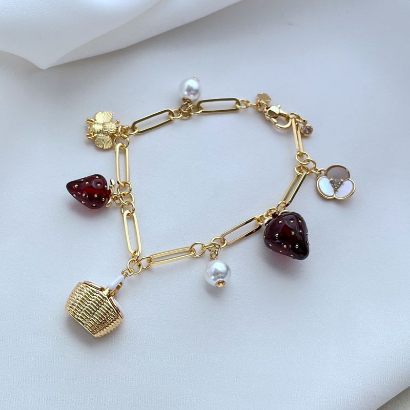  Bracelet displayed on a red gingham or soft cream background, evoking a classic picnic aesthetic. Alt: “Kate Spade Picnic Basket and Strawberry Bracelet – Summer Enamel Charm Jewelry.”