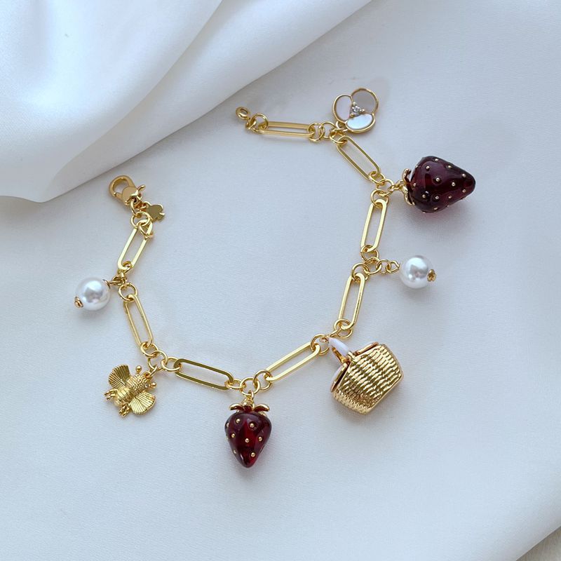  Bracelet displayed on a red gingham or soft cream background, evoking a classic picnic aesthetic. Alt: “Kate Spade Picnic Basket and Strawberry Bracelet – Summer Enamel Charm Jewelry.”