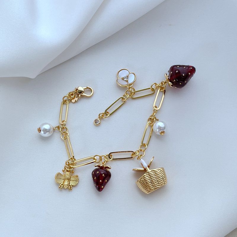  Bracelet displayed on a red gingham or soft cream background, evoking a classic picnic aesthetic. Alt: “Kate Spade Picnic Basket and Strawberry Bracelet – Summer Enamel Charm Jewelry.”