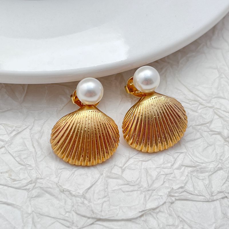 Earrings on a soft sand-beige or seafoam green background, showcasing the sculpted gold shell with pearl or crystal center. Alt: “Kate Spade Reef Treasure Shell Stud Earrings – Gold Seashell Nautical Jewelry.”