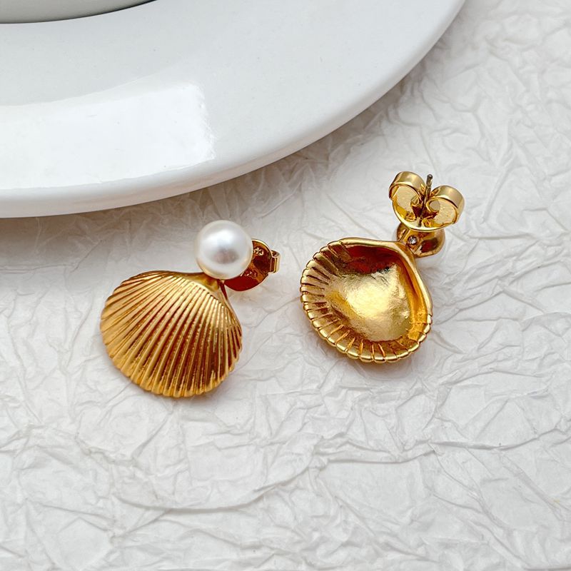 Earrings on a soft sand-beige or seafoam green background, showcasing the sculpted gold shell with pearl or crystal center. Alt: “Kate Spade Reef Treasure Shell Stud Earrings – Gold Seashell Nautical Jewelry.”