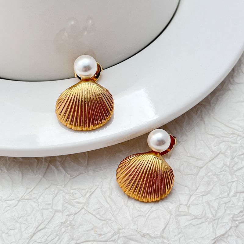 Earrings on a soft sand-beige or seafoam green background, showcasing the sculpted gold shell with pearl or crystal center. Alt: “Kate Spade Reef Treasure Shell Stud Earrings – Gold Seashell Nautical Jewelry.”