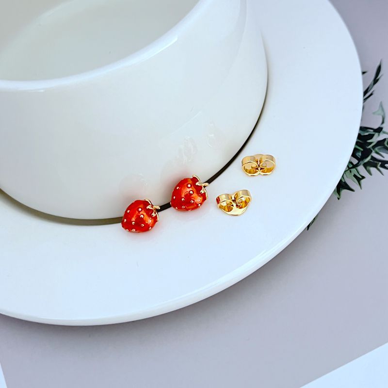  Macro focus on one strawberry stud, showing the red enamel, green leaf detail, and golden seed accents. Alt: “Red Enamel Strawberry with Gold Seed Detail – Kate Spade Earrings.”