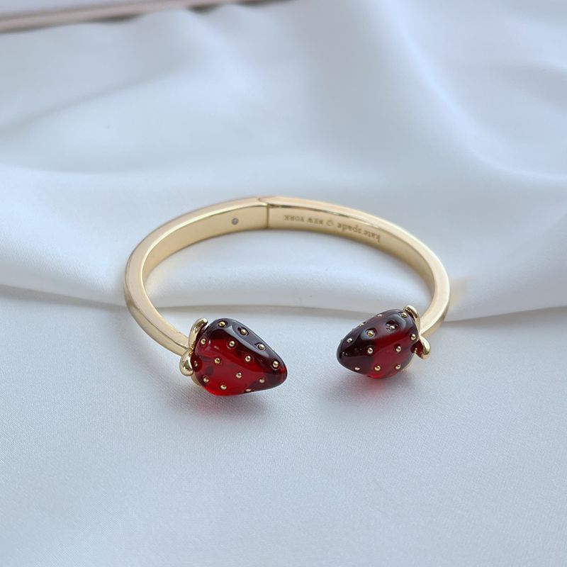 Bracelet on a light, natural background (white wood or pale pink), highlighting the strawberry enamel details. Alt: “Kate Spade Strawberry Gold Bracelet – Dainty Fruit Charm Jewelry.”