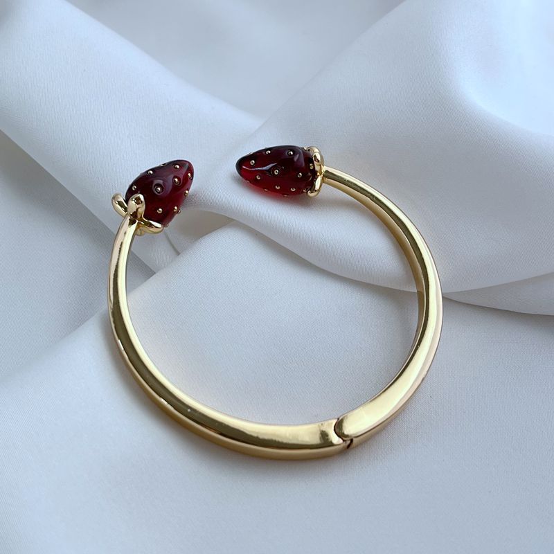 Bracelet on a light, natural background (white wood or pale pink), highlighting the strawberry enamel details. Alt: “Kate Spade Strawberry Gold Bracelet – Dainty Fruit Charm Jewelry.”