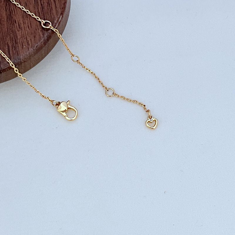 Macro shot focused on one of the heart charms and the fine chain links, highlighting the polished finish.