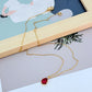 Necklace displayed on a dark background (navy or charcoal) to make the gold and fuchsia gemstone pop. Alt: “Kate Spade Treasure Trove Gold Necklace with Fuchsia Gem – Bold Statement Pendant.”