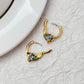 Earrings on a soft aquatic blue or seafoam green background, showcasing the gold huggie hoop with dangling enamel fish charm. Alt: “Kate Spade What A Catch Fish Huggie Earrings NEW – Gold Fish Hoop Jewelry.”