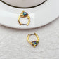 Earrings on a soft aquatic blue or seafoam green background, showcasing the gold huggie hoop with dangling enamel fish charm. Alt: “Kate Spade What A Catch Fish Huggie Earrings NEW – Gold Fish Hoop Jewelry.”