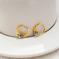 Earrings on a soft aquatic blue or seafoam green background, showcasing the gold huggie hoop with dangling enamel fish charm. Alt: “Kate Spade What A Catch Fish Huggie Earrings NEW – Gold Fish Hoop Jewelry.”