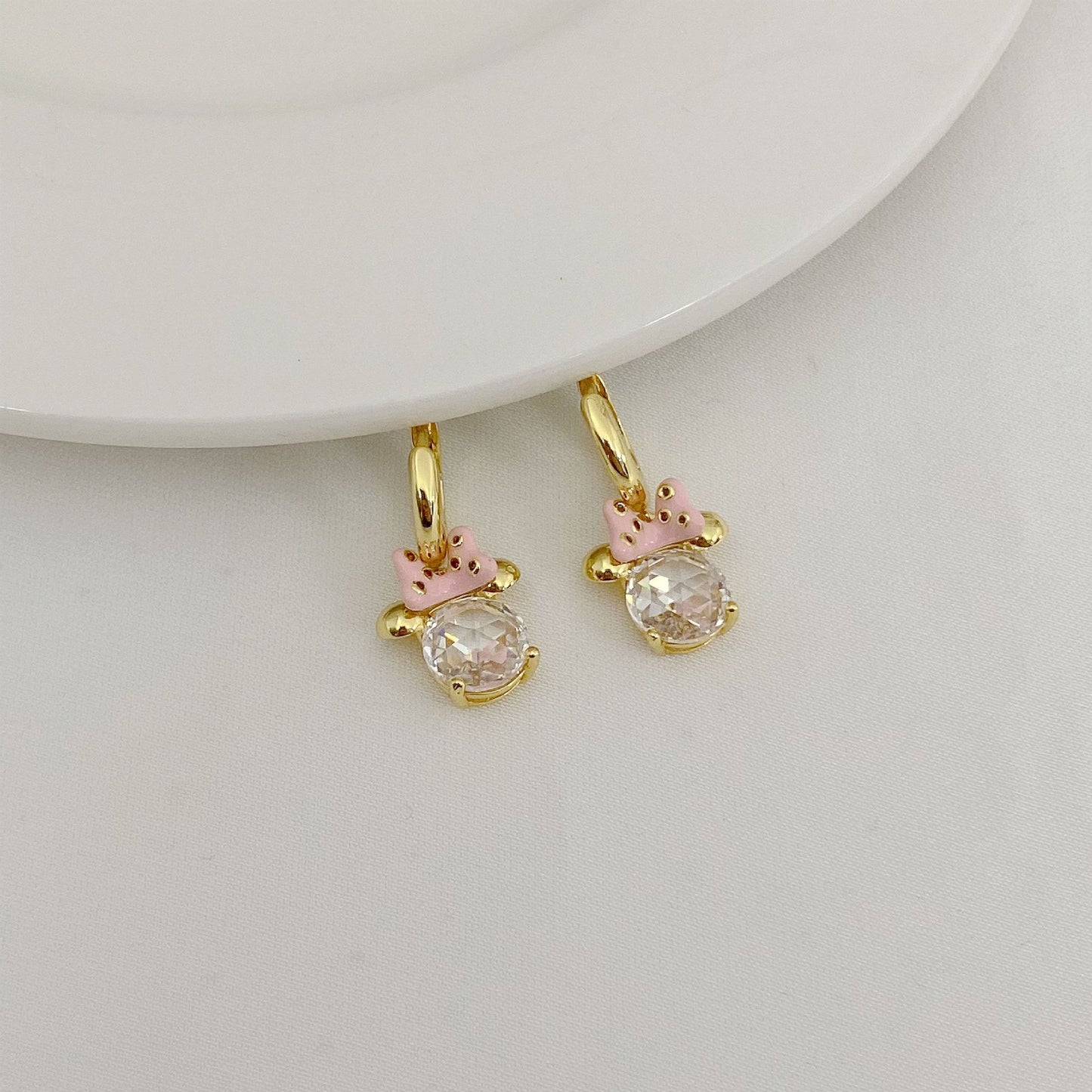 Gold hoop earrings with pink accents and clear gemstones on a light gray background