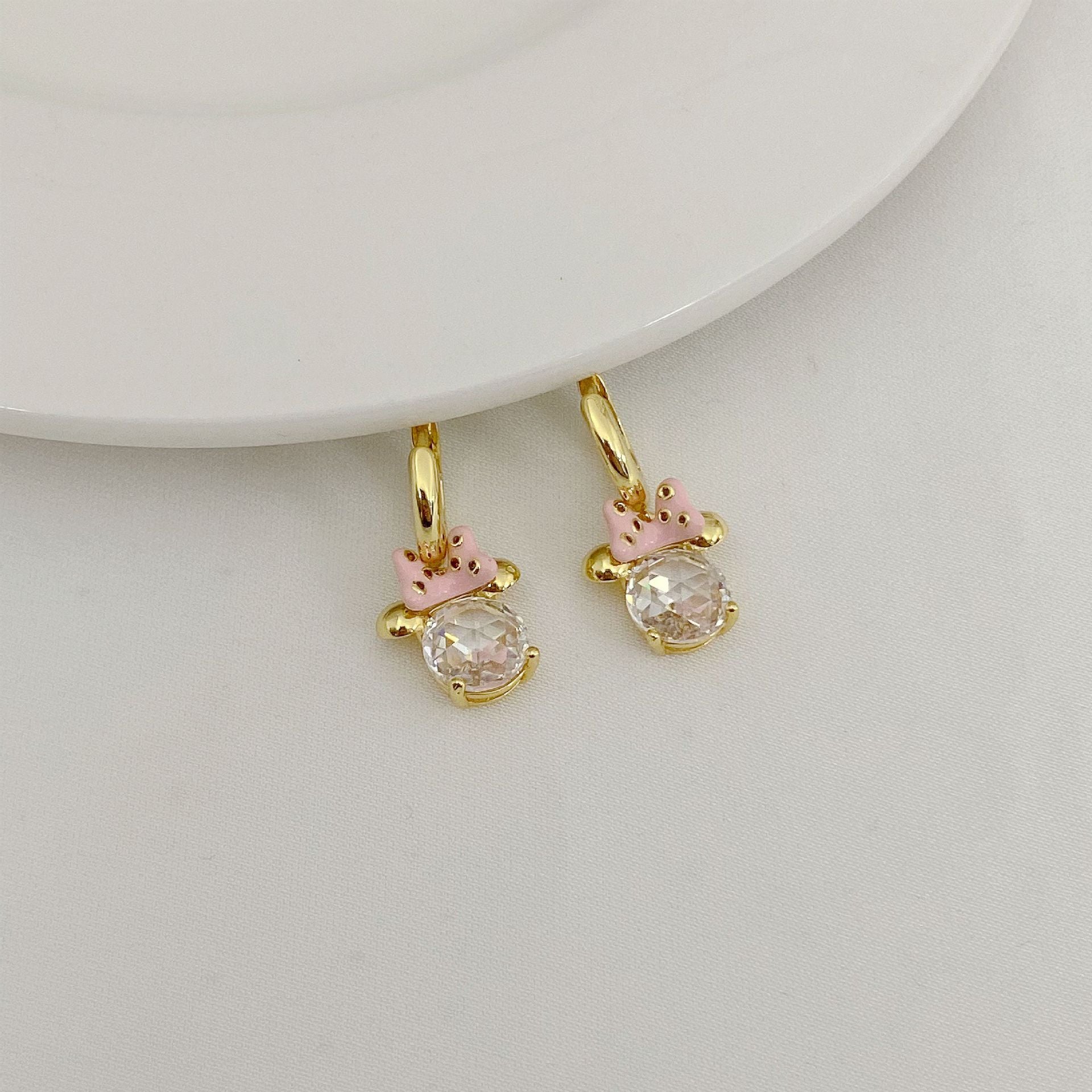 Gold hoop earrings with pink accents and clear gemstones on a light gray background