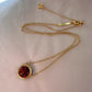 Gold necklace with a red pendant on a light pink background