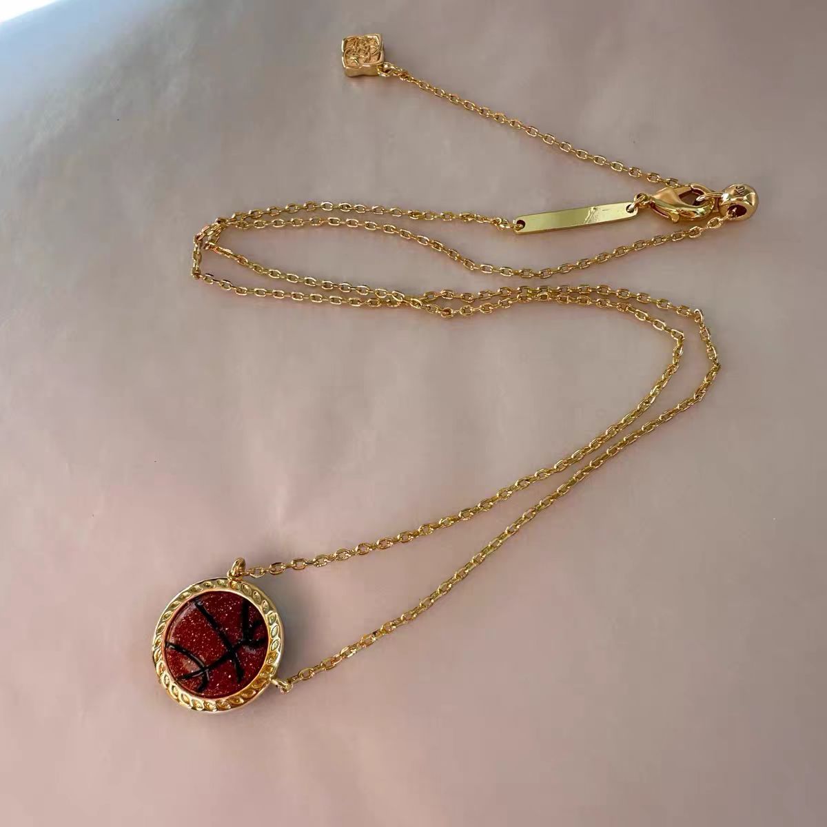 Gold necklace with a red pendant on a light pink background