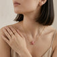 A close-up lifestyle shot of a model wearing a delicate gold chain necklace with a pink starfish pendant, paired with gold rings and a small gold hoop earring.