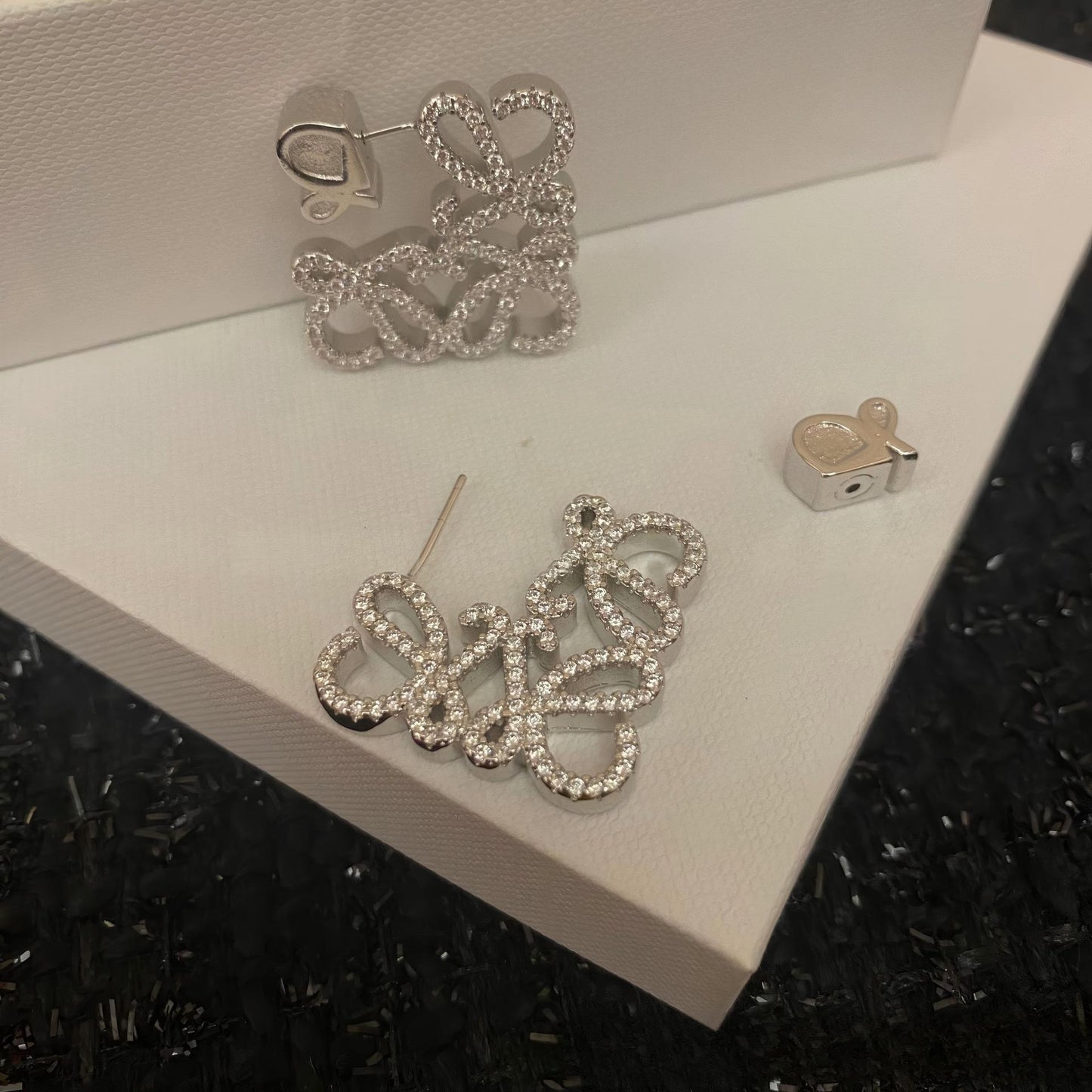 Clear, high-resolution front view of the Loewe-style pavé anagram stud earrings on a neutral background. Highlight the sparkling crystal accents and gold tone finish.