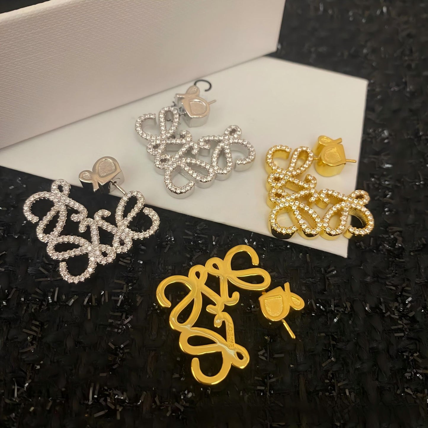 Clear, high-resolution front view of the Loewe-style pavé anagram stud earrings on a neutral background. Highlight the sparkling crystal accents and gold tone finish.
