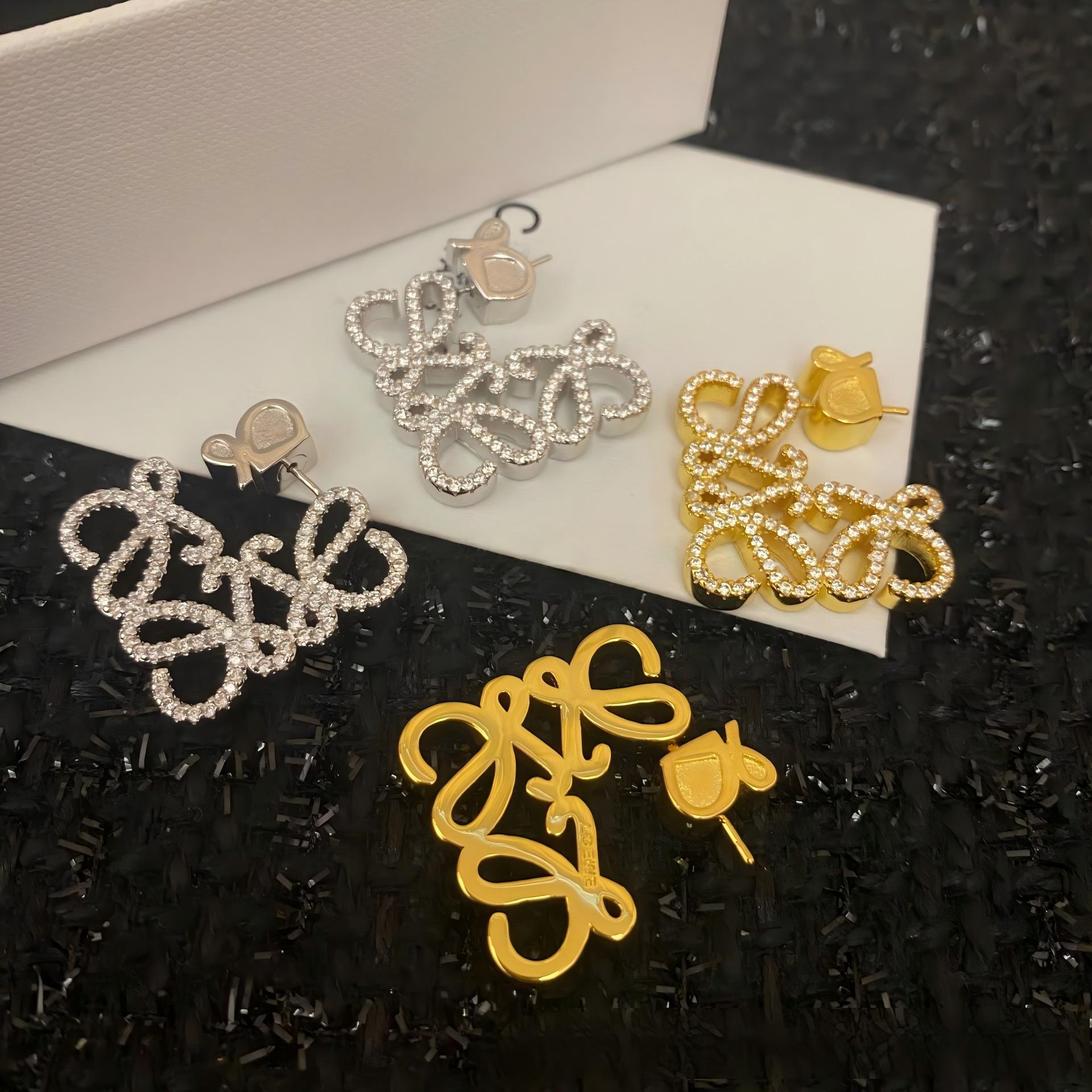 Clear, high-resolution front view of the Loewe-style pavé anagram stud earrings on a neutral background. Highlight the sparkling crystal accents and gold tone finish.