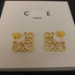 Clear, high-resolution front view of the Loewe-style pavé anagram stud earrings on a neutral background. Highlight the sparkling crystal accents and gold tone finish.