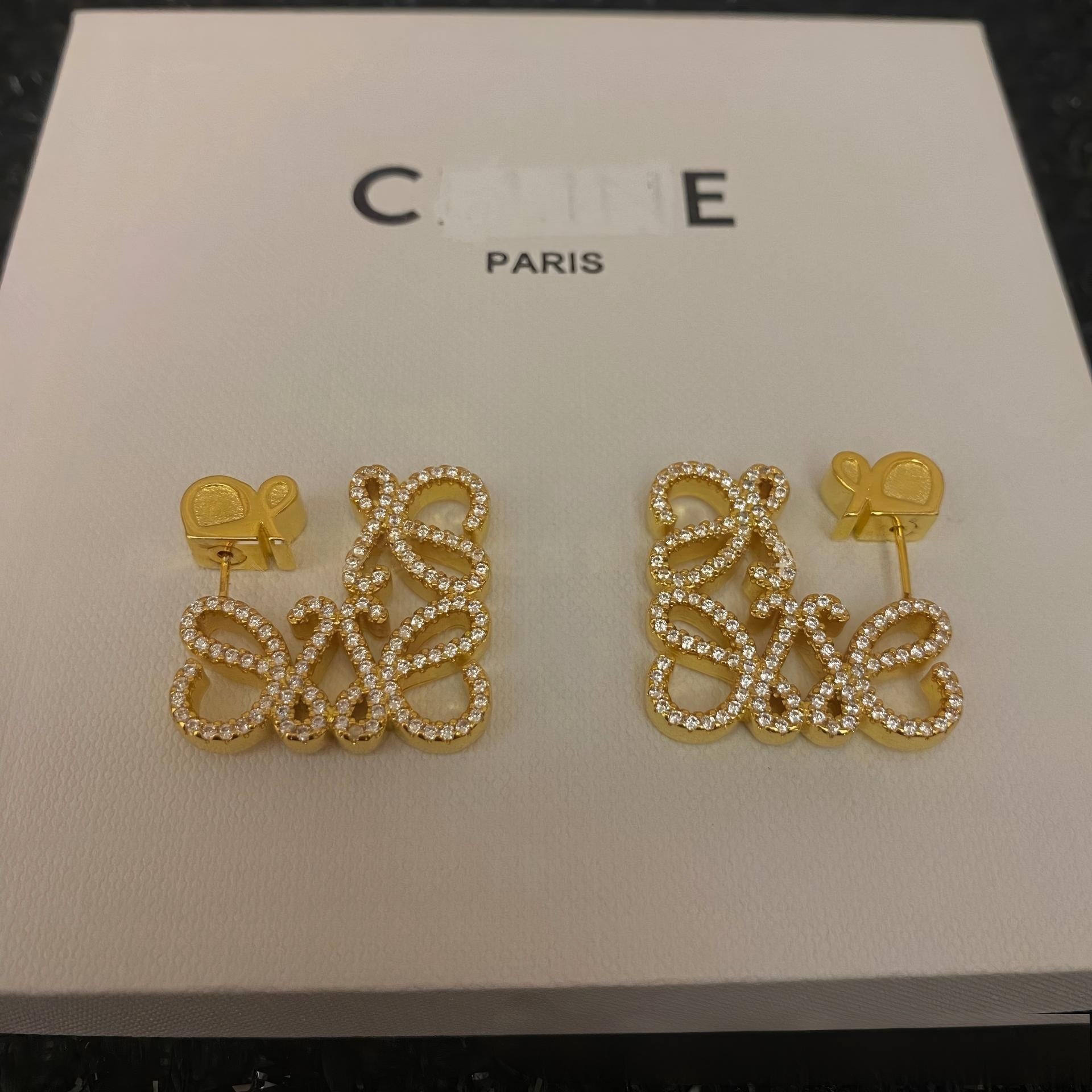 Clear, high-resolution front view of the Loewe-style pavé anagram stud earrings on a neutral background. Highlight the sparkling crystal accents and gold tone finish.
