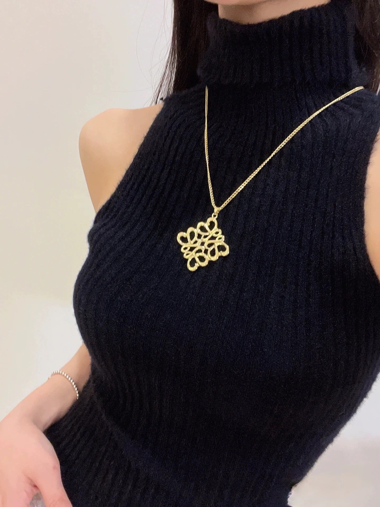The necklace draped over a folded knit sweater or on a vanity next to a Loewe candle, reinforcing its association with cozy luxury and modern style.