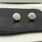 Clean shot of a single earring against a neutral, textured background (like linen or stone), highlighting the smooth pebble shape and integrated logo.