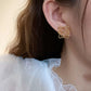 An editorial close-up of the earrings being worn, emphasizing their modern, architectural appeal against the skin.