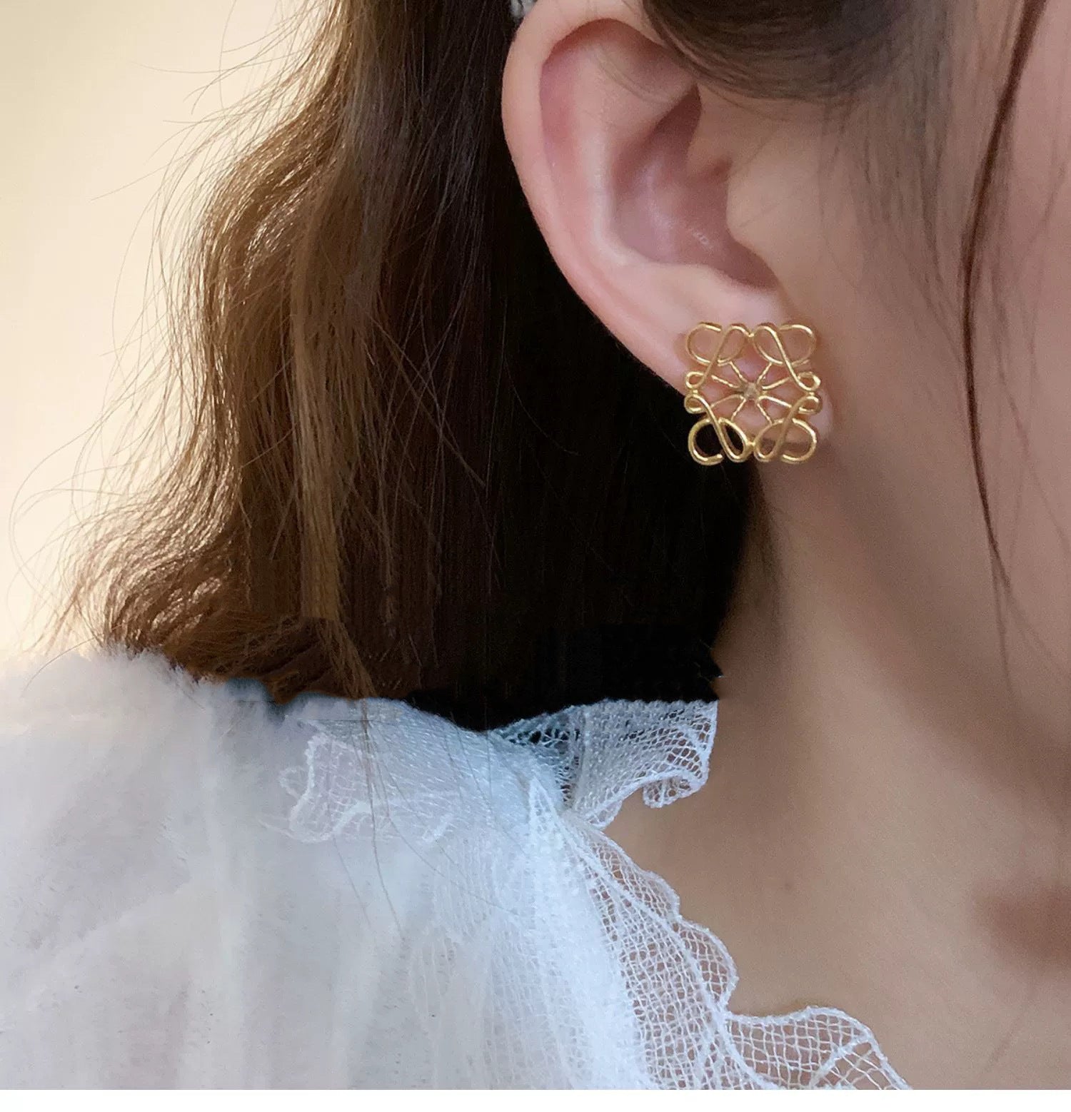 An editorial close-up of the earrings being worn, emphasizing their modern, architectural appeal against the skin.