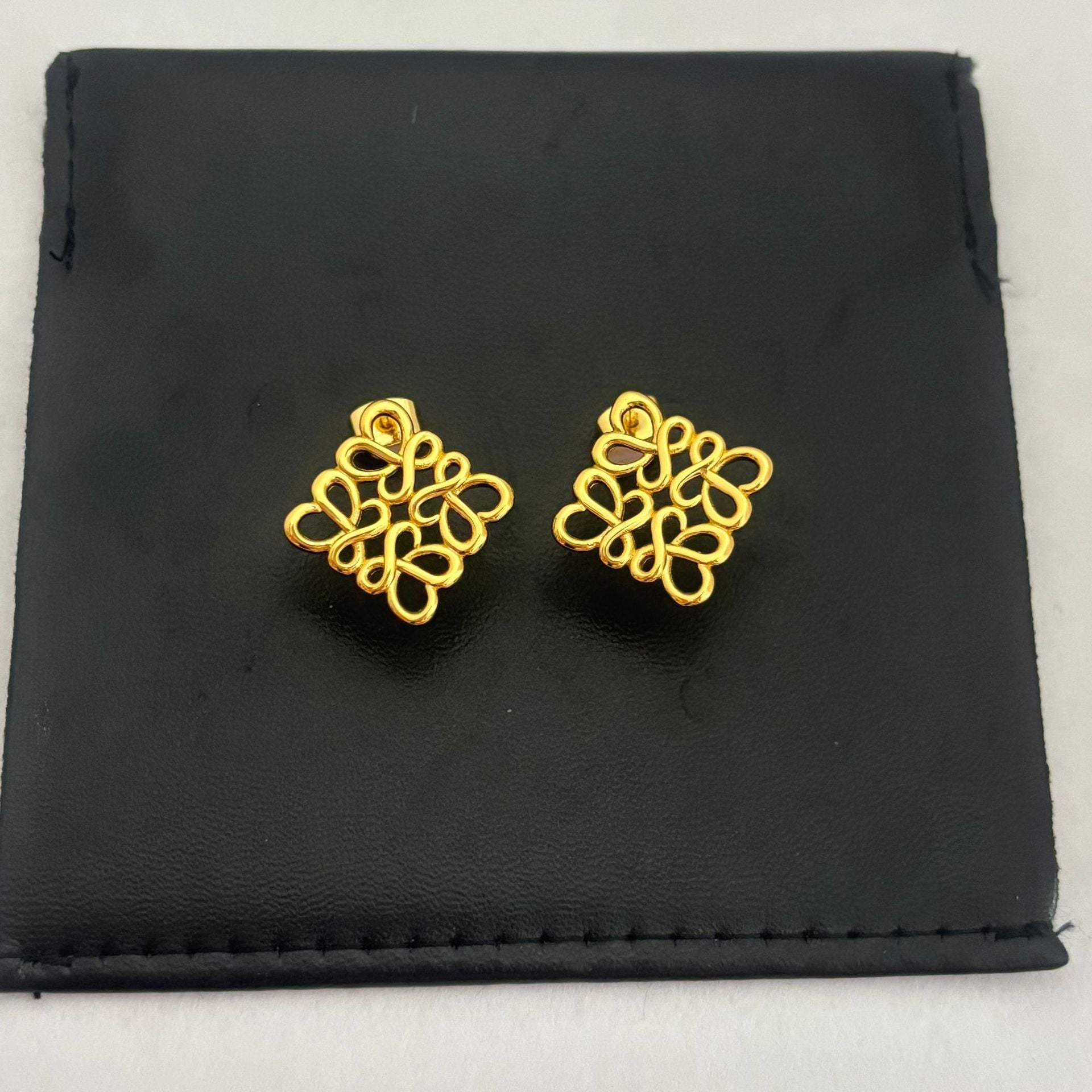 Clean, direct shot of a single earring against a neutral background, highlighting the smooth rhombus shape and the intricate openwork logo.