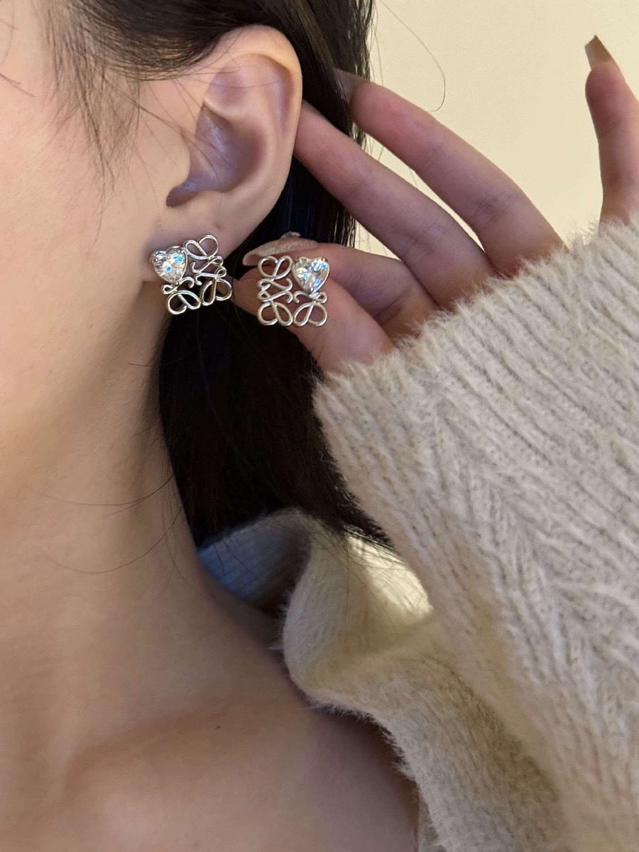The earrings placed next to a simple line drawing of two hearts or on a page of poetry, reinforcing the themes of love and meaningful design.