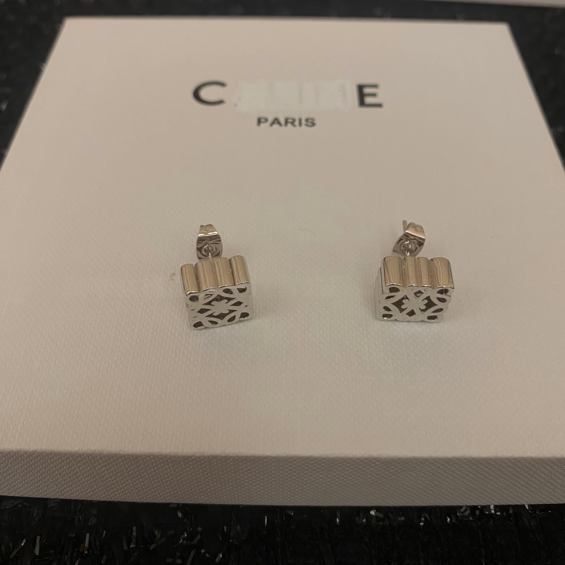 Clean, front-facing shot of the geometric hoop earrings on a plain background, highlighting the intricate gold tone design.
