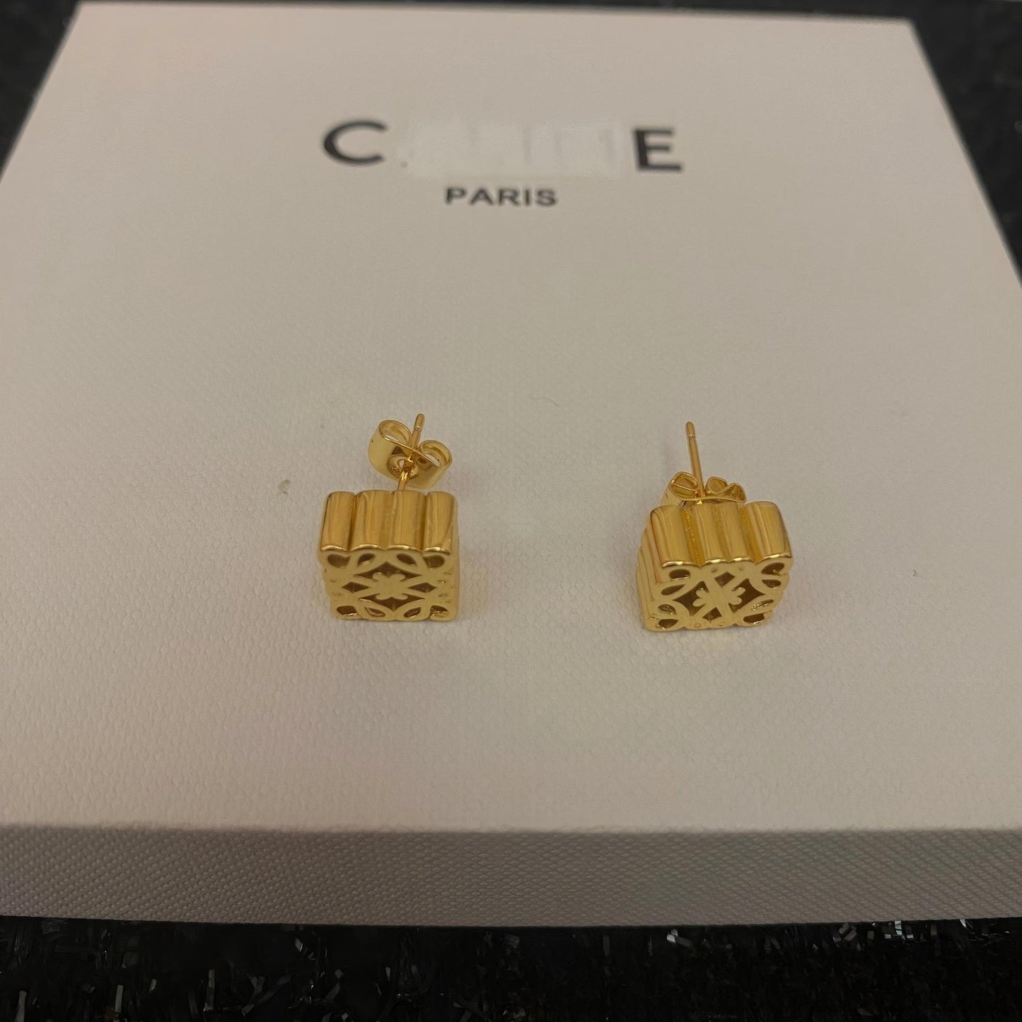 Clean, front-facing shot of the geometric hoop earrings on a plain background, highlighting the intricate gold tone design.