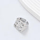 Clean, angled shot of the ring on a finger or stand, showcasing the square silhouette and intricate hollow pattern against a solid background.