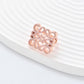 Clean, angled shot of the ring on a finger or stand, showcasing the square silhouette and intricate hollow pattern against a solid background.
