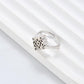 Clean, angled shot of the ring on a finger or stand, showcasing the square silhouette and intricate hollow pattern against a solid background.